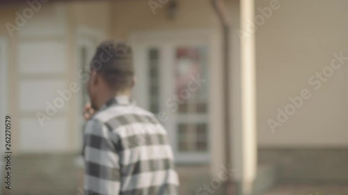 Portrait of handsome african american man in checkered shirt demonstrating the keys in front of a big house. The man turns and walks to the door of his new home. The guy just bought house