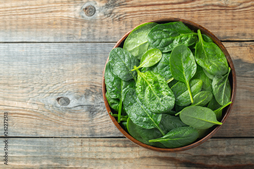 Fresh spinach leaves in bowl on rustic wooden table. Top view