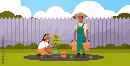 couple farmers planting young tree african american man holding water buckets woman digging soil working in garden agricultural gardening concept backyard background full length horizontal