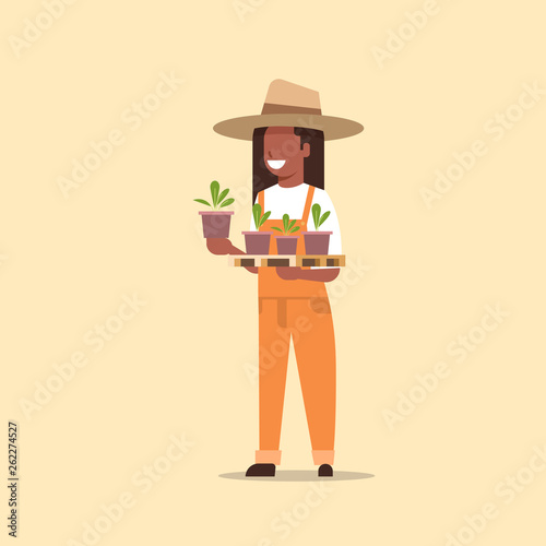 female farmer holding potted plants african american woman in uniform planting young seedlings in garden agricultural worker eco farming concept flat full length