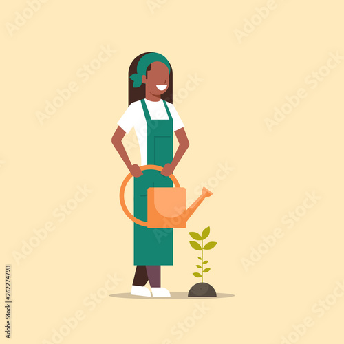 female farmer growing seedling plant flower or vegetable african american woman holding watering can gardener in uniform agricultural eco farming concept flat full length
