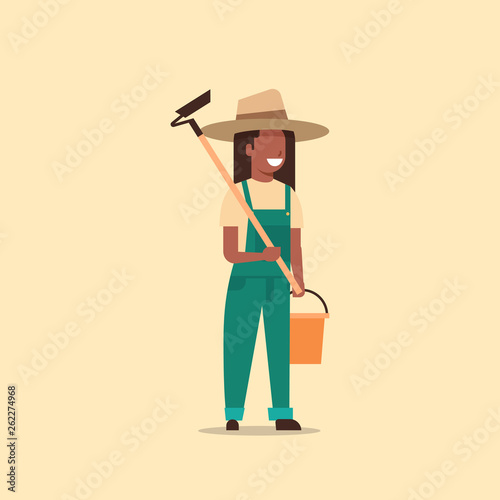 female gardener holding hoe and bucket african american country woman working in garden gardening eco farming concept full length