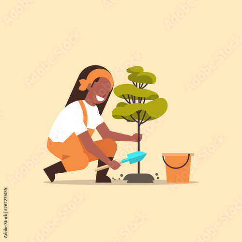 female farmer planting young tree african american gardener woman digging soil working in garden agricultural gardening concept flat full length