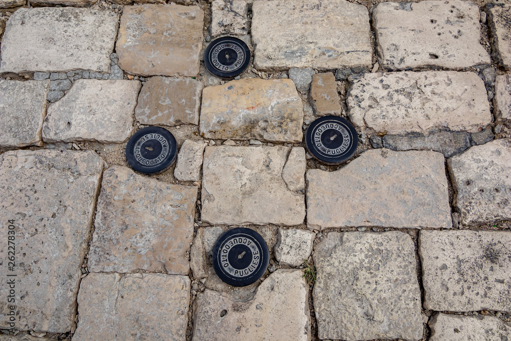 Four small black iron manhole covers in Matera, Italy, Public stone paved street in the old town. Moody summer day