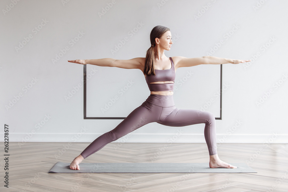 Naklejka premium Beautiful woman doing yoga at home and doing the pose of the hero. The concept of home workouts and body maintenance. Place for advertising