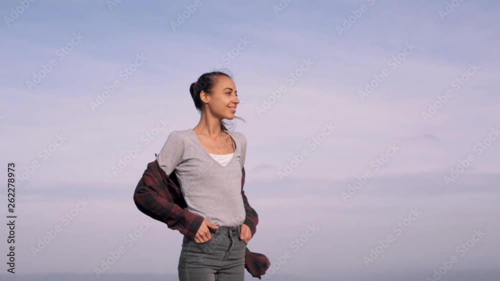 young female hiker is walking on edge of mountain ridge against background of sunset sky. Woman is hiking in mountains before sunset. strong wind is fluttering woman's hair and shirt young female hiker is walking on edge of mountain ridge against background of sunset sky. Woman is hiking in mountains before sunset. strong wind is fluttering woman's hair and shirt