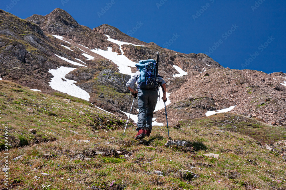 A mountaineer equipped for a climb, climbs a mountain path with difficulty