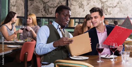 Сheerful male friends choosing dishes from menu card in restaurant photo