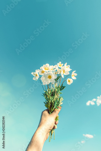 Creative layout whis flowers in hand against a bright blue sky. Summer background concept.