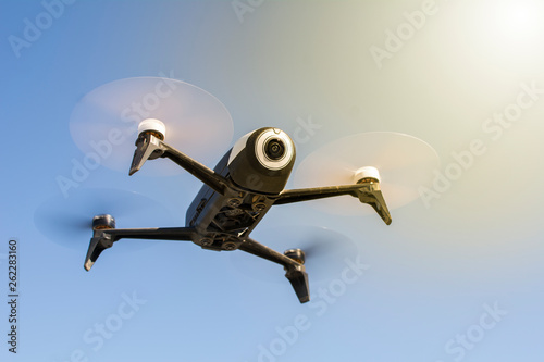 Drone, aircraft that flies without crew, with remote control. Low angle. Blue sky and sunbeam in the background.