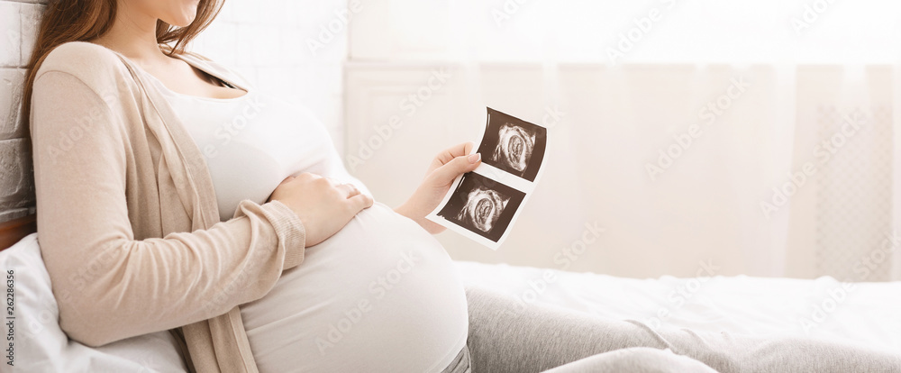 Pregnant woman holding ultrasound image lying in bed - obrazy, fototapety, plakaty 