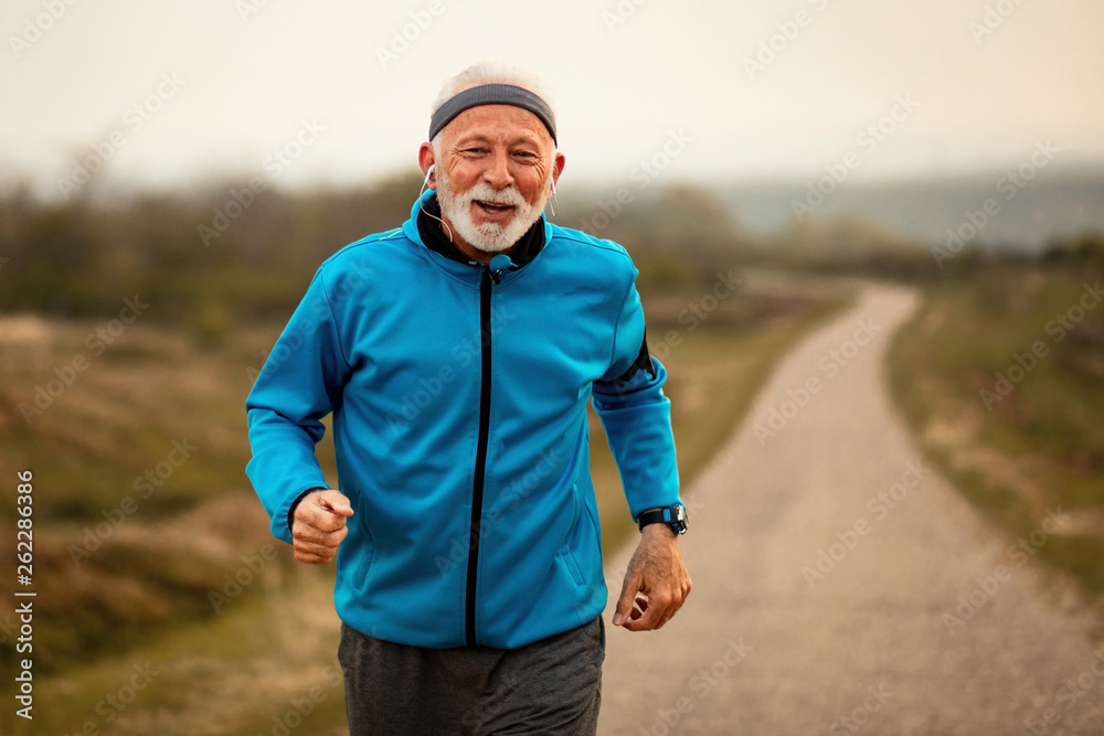 Fototapeta premium Motivated mature athlete jogging and listening music on earphones.