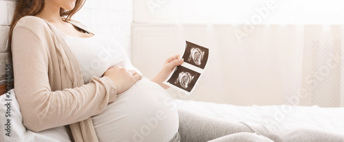 Pregnant woman holding ultrasound image lying in bed