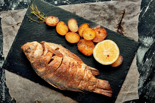 Grilled whole fish Served with baked potatoes, lemon and sauce. Top view.