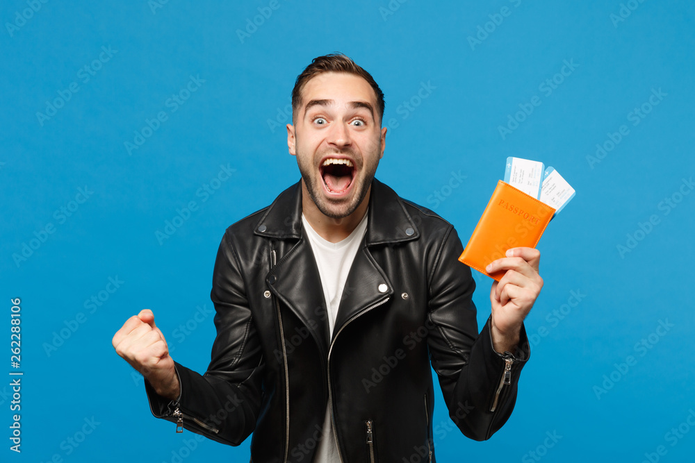 Young happy unshaven man in black jacket white t-shirt hold in hand passport tickets isolated on blue wall background. Passenger traveling abroad getaway. Air flight journey concept Mock up copy space Young happy unshaven man in black jacket white t-shirt hold in hand passport tickets isolated on blue wall background. Passenger traveling abroad getaway. Air flight journey concept Mock up copy space