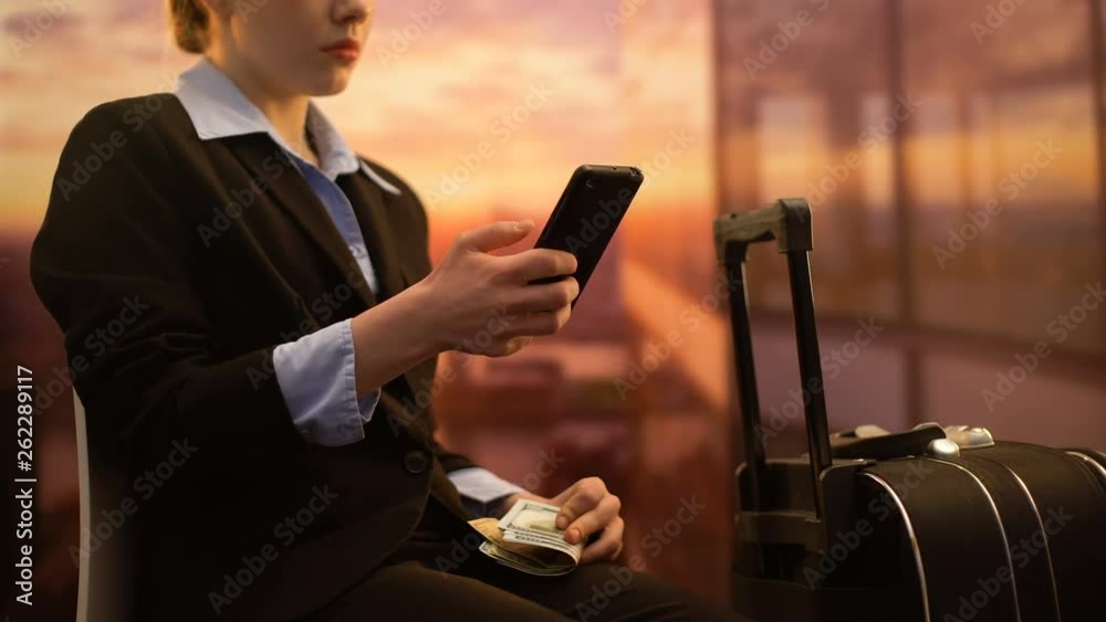 Businesswoman sitting in airport and using cellphone app to count money for trip