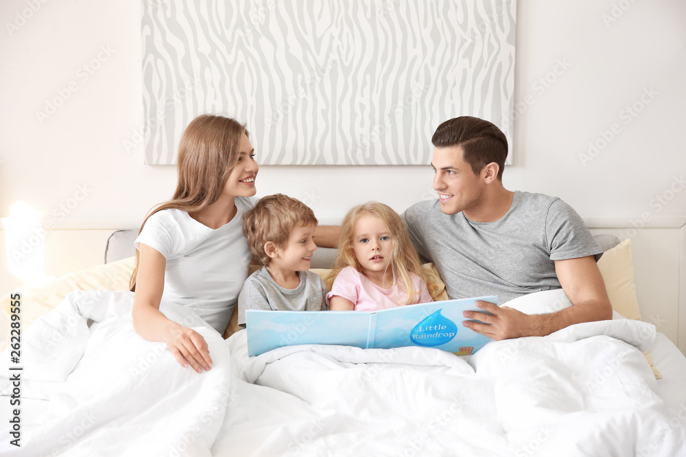 Fototapeta premium Happy family reading book in bed at home