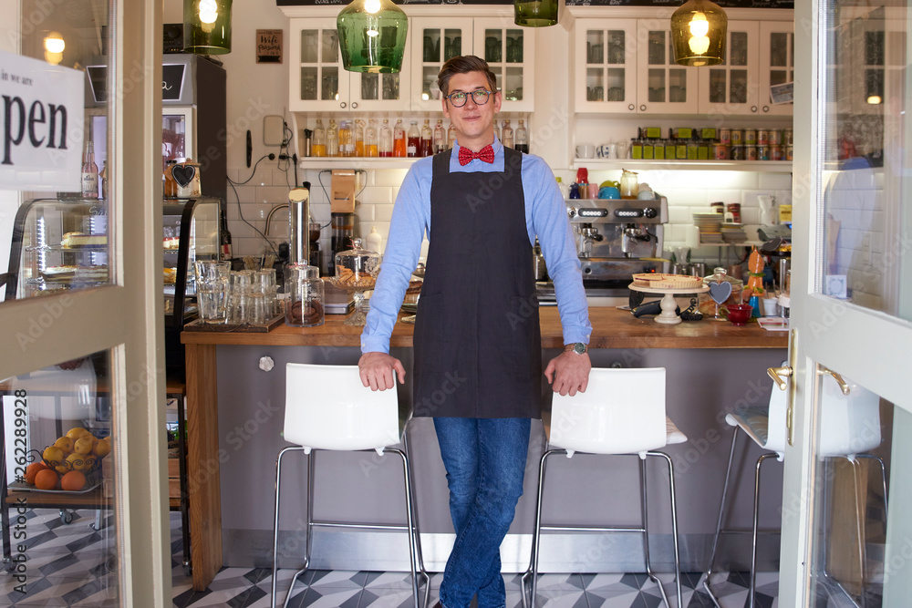 Confident young coffee shop owner man standing in cafe and waiting for guest