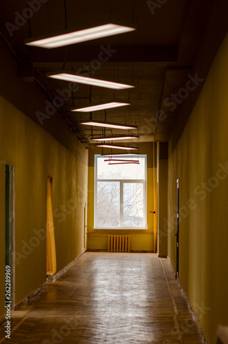 Old corridor of times of the USSR with shabby yellow walls, wooden window and linoleum. Doorways without doors. rectangular white lamps on the ceiling. The atmosphere of horror movies.