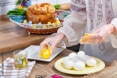 Woman s hands are painting eggs in yellow color on the working surface.
