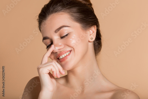 Happy smiling girl with perfect skin with moisturizing face cream on a cheek. Skin care and health concept.
