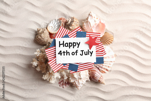 Flat lay composition with greeting card, USA flags and seashells on sand. Happy Independence Day photo