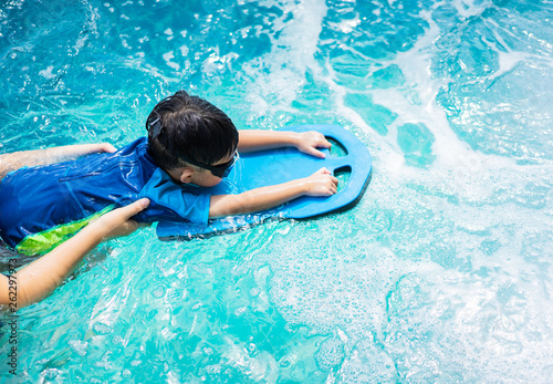 A boy is swimming with kickboard and swimming goggles.