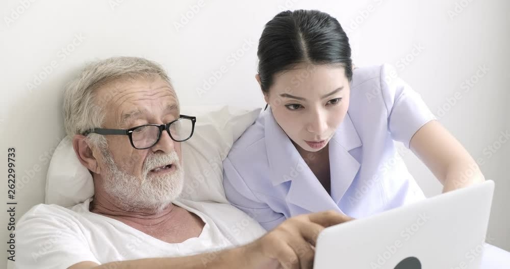 Senior man in bed with nurse using laptop. White male and asian female. Focusing on teaching him. Senior lifestyle concept. Senior man in bed with nurse using laptop. White male and asian female. Focusing on teaching him. Senior lifestyle concept.