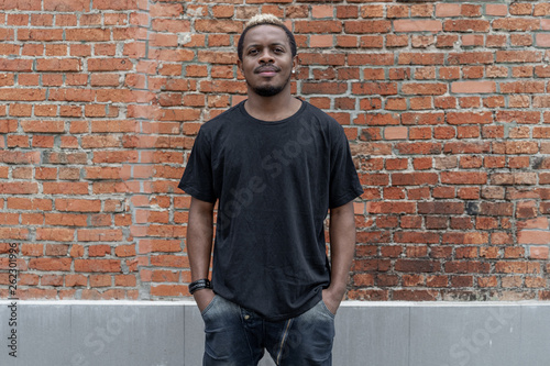 Young attractive dark-skinned man in black T-shirt on red bricked background.