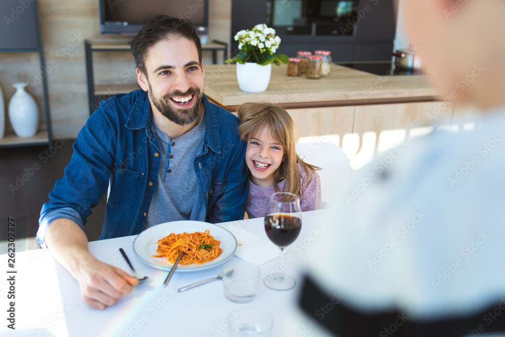 Handsome young father and her beautiful having fun while eating pasta with tomatoe sauce for lunch in the kitchen at home.