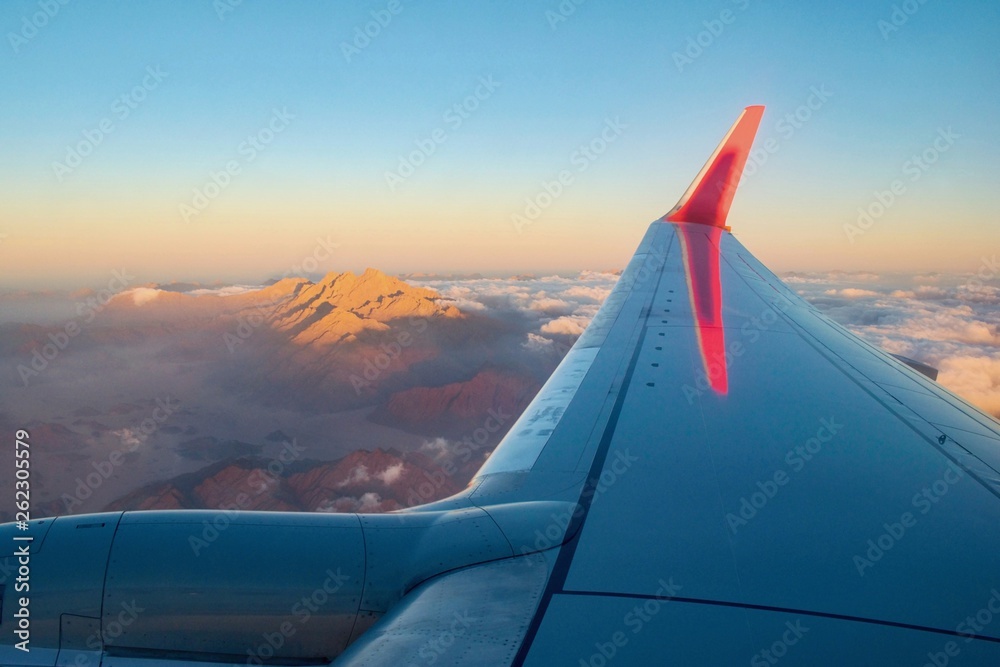 Aircraft flying above Sahara desert mountains within sunrise