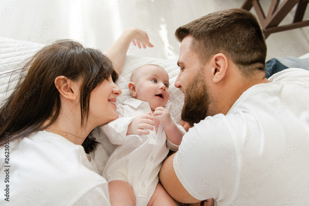 Happy smiling young family in bed with infant Happy smiling young family in bed with infant