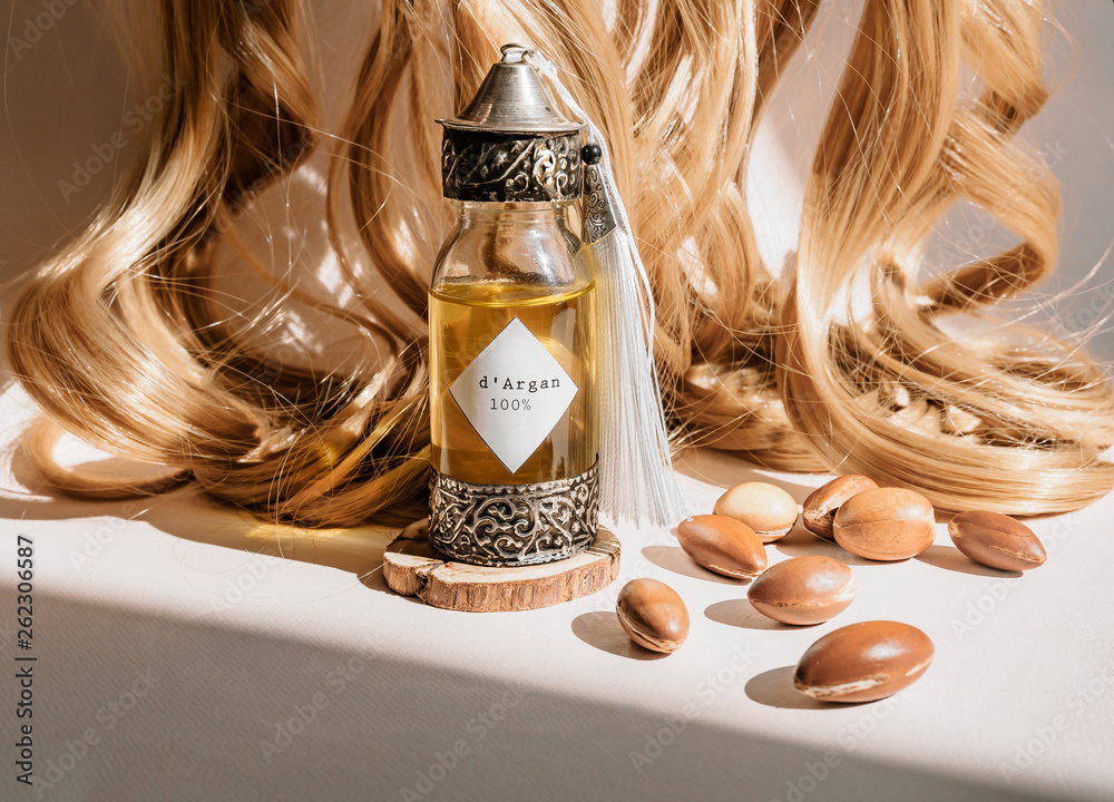 Curls of golden hair and decorative bottle with iron embossed in  traditional Moroccan style with precious Moroccan argan oil and nuts ander  natural lighting of sun with hadows frame Stock Photo |