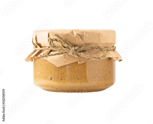 Side view of glass jar with nut butter, hummus or sesame paste tahini with paper covered cap. Food ingredient isolated on white background