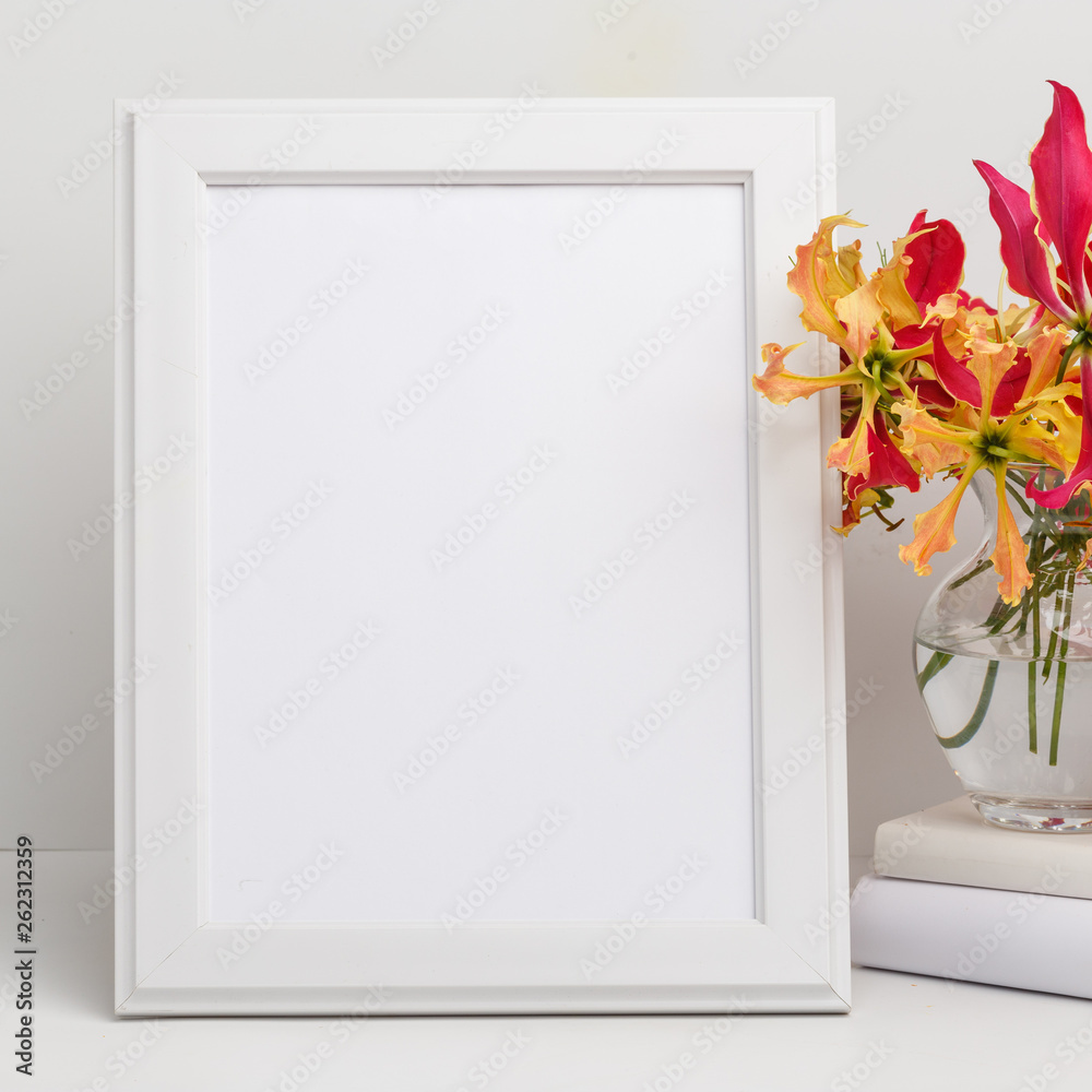 Composition from a decorative wooden frame and red and yellow flowers of Glorios in a glass vase on a white shelf Composition from a decorative wooden frame and red and yellow flowers of Glorios in a glass vase on a white shelf