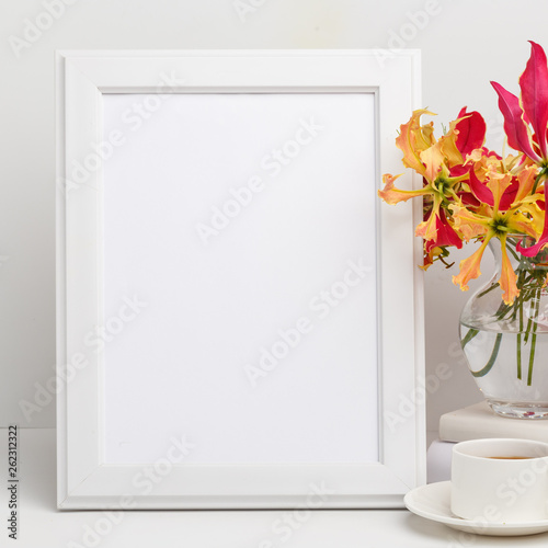 Composition from a decorative wooden frame and red and yellow flowers of Glorios in a glass vase on a white shelf