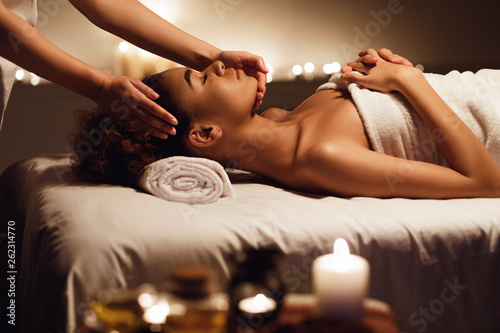 African girl having face massage, relaxing in spa salon