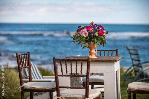 An antique table and chairs with a beautiful bouquet of flowers in a vase with the ocean in the background