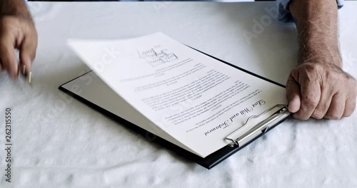 Senior man signing his last will and testament in dining table, focus and moody pose. White male.
