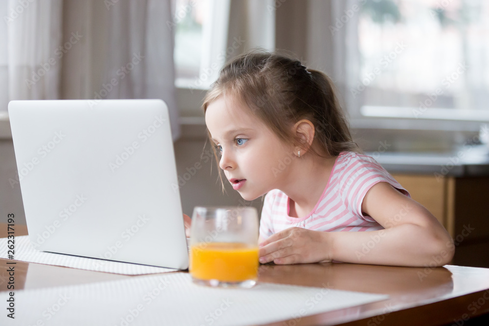 Little girl busy playing computer in kitchen at home Little girl busy playing computer in kitchen at home
