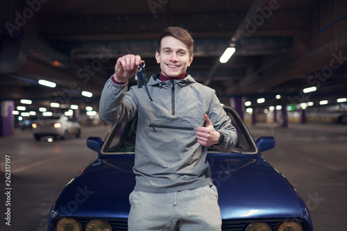 Photo of man with keys standing by car in underground parking. © Sergey