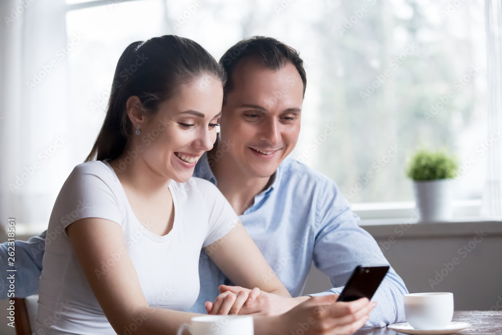 Smiling couple reading funny message on phone at home Smiling couple reading funny message on phone at home