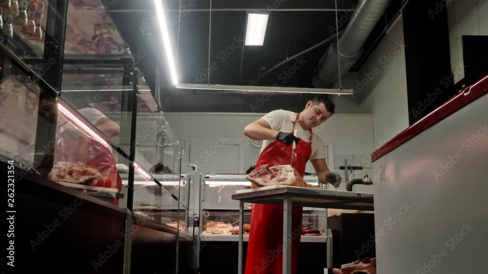 butcher in red apron and black gloves cuts huge meat piece