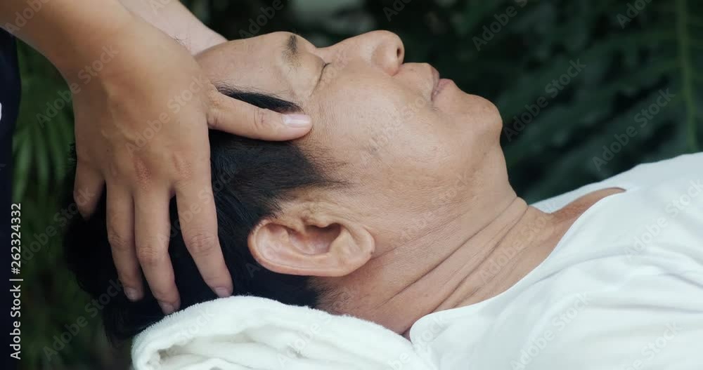 Senior man having head massage outdoor. Asian male laying in bed. Side shot. Senior lifestyle.