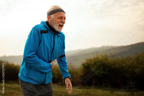 Active mature athlete feeling pain while jogging in nature.