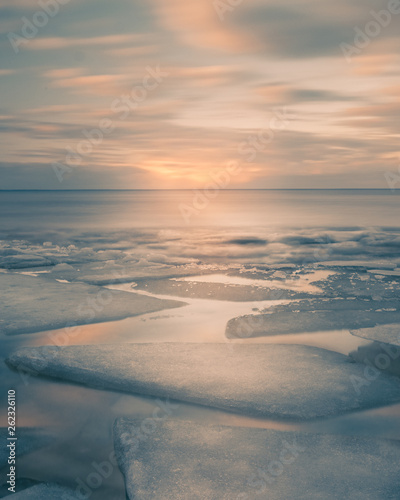 Sunset on the Kyiv Sea at wintertime with broken ice cracks in Golden Hour with beautiful clouds. Pack Ice builds up the icebergs. Ukraine