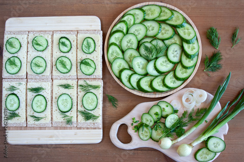  Light, spring sandwiches with cheese, fresh cucumber and dill, next to a tray with slices of cucumber and a board full of green spring vegetables