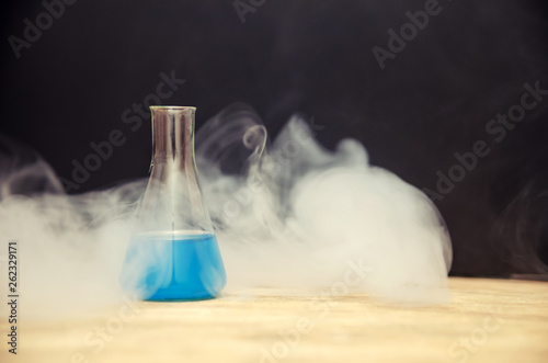 flask with blue liquid in smoke over black background. chemical analysis
