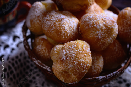 Fresh handmade profiteroles in a wicker basket on a lace doily in a ray of light, macro