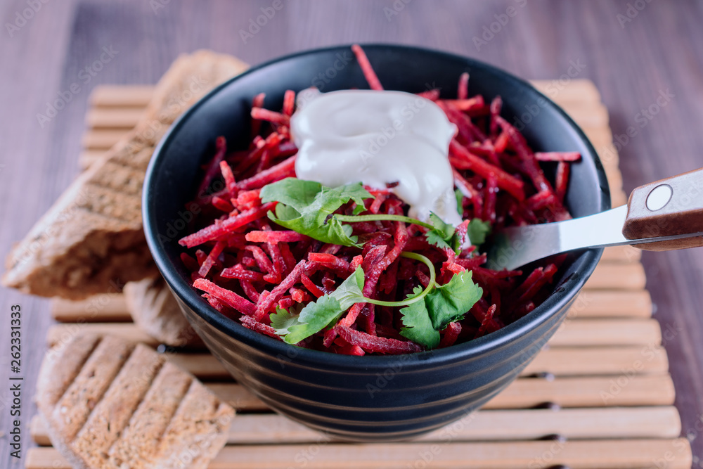 Thinly sliced fresh beets in a black salad bowl with sprigs of cilantro ready for eating are on a wooden table, closeup. Thinly sliced fresh beets in a black salad bowl with sprigs of cilantro ready for eating are on a wooden table, closeup.